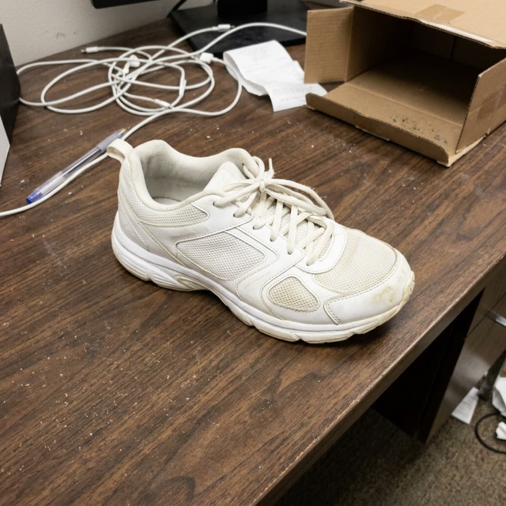 A plain supplier product photo of a running shoe on a cluttered desk.
